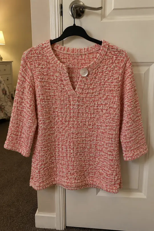 A real phone photo: a coral knit top on a hanger on a bedroom door